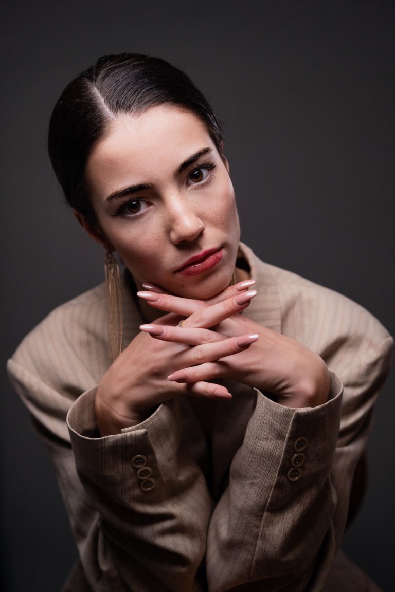 Une mannequin photographiée en studio sur fond gris. Elle est assise et porte une veste de costume.