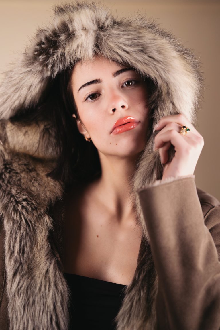Portrait d'une mannequin photographiée en studio sur fond crème. Elle porte un manteau de fourrure.