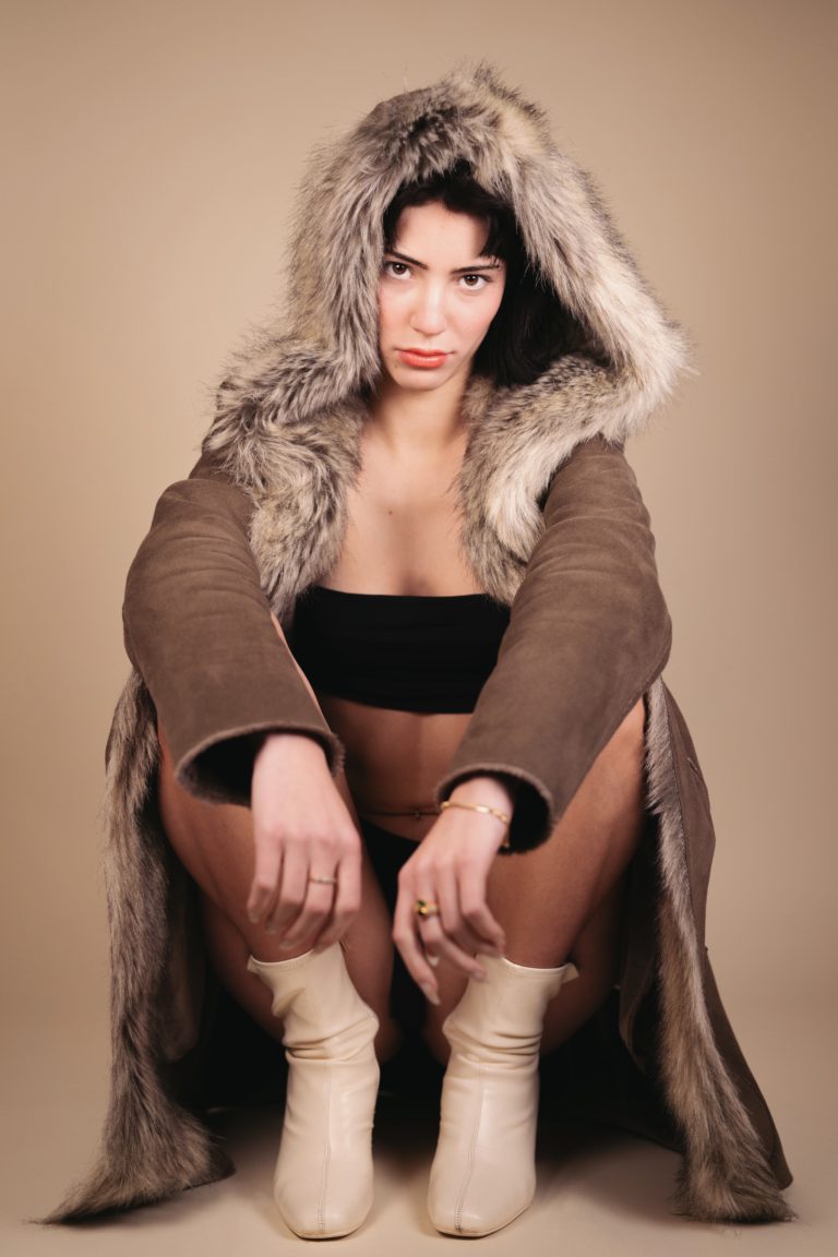 Une mannequin photographiée en studio sur fond crème. Elle porte un manteau de fourrure.