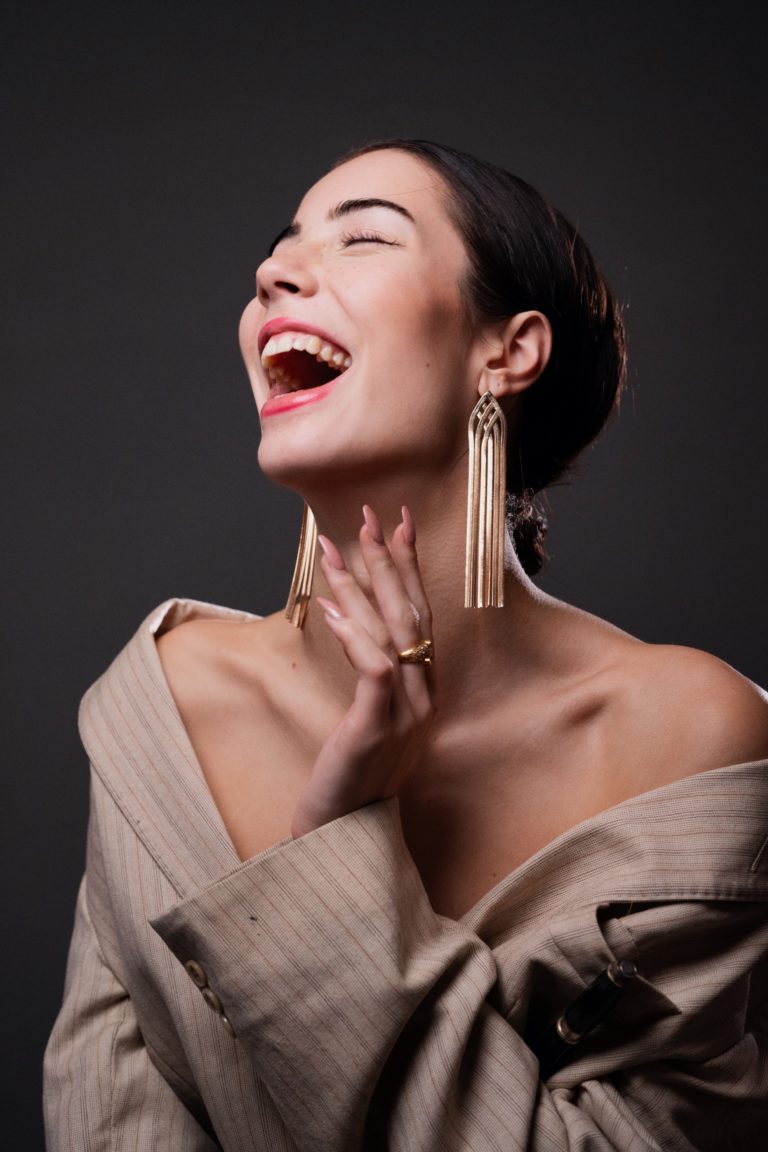 Une mannequin photographiée en studio sur fond gris. Elle rit et porte une veste de costume.