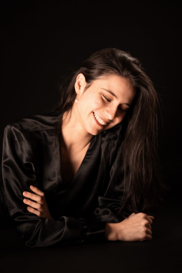 Une jeune femme vêtue de noir photographiée en studio sur fond noir, elle sourit