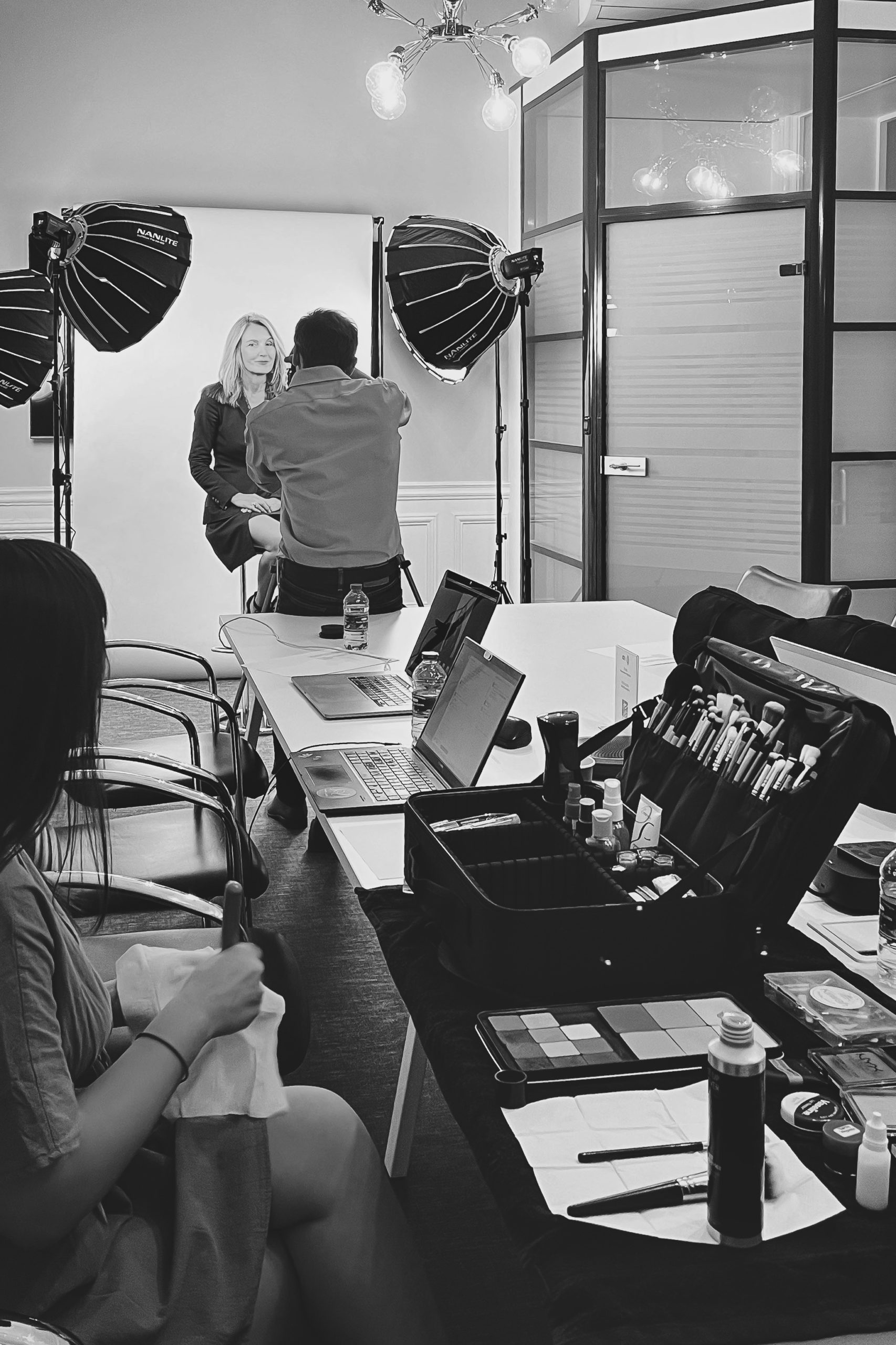 Photographe de dos prenant des photos de portrait dans un studio mobile installé dans un cabinet d'avocats à Paris. La maquilleuse regarde la scène.