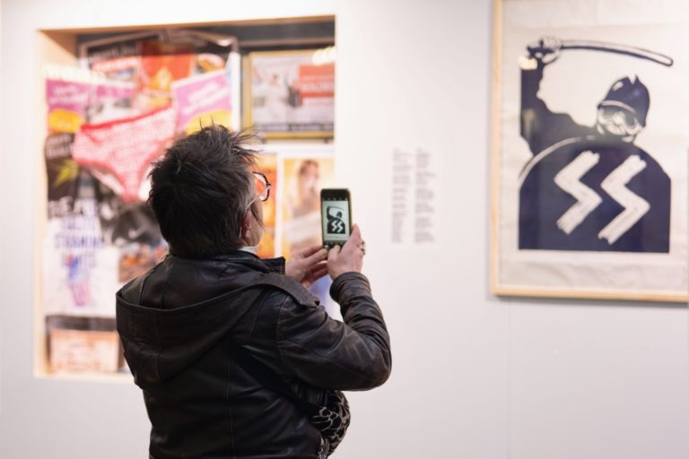 Photographie de l'exposition "Détournements" à Ground Control, une femme prend une oeuvre en photo avec son téléphone